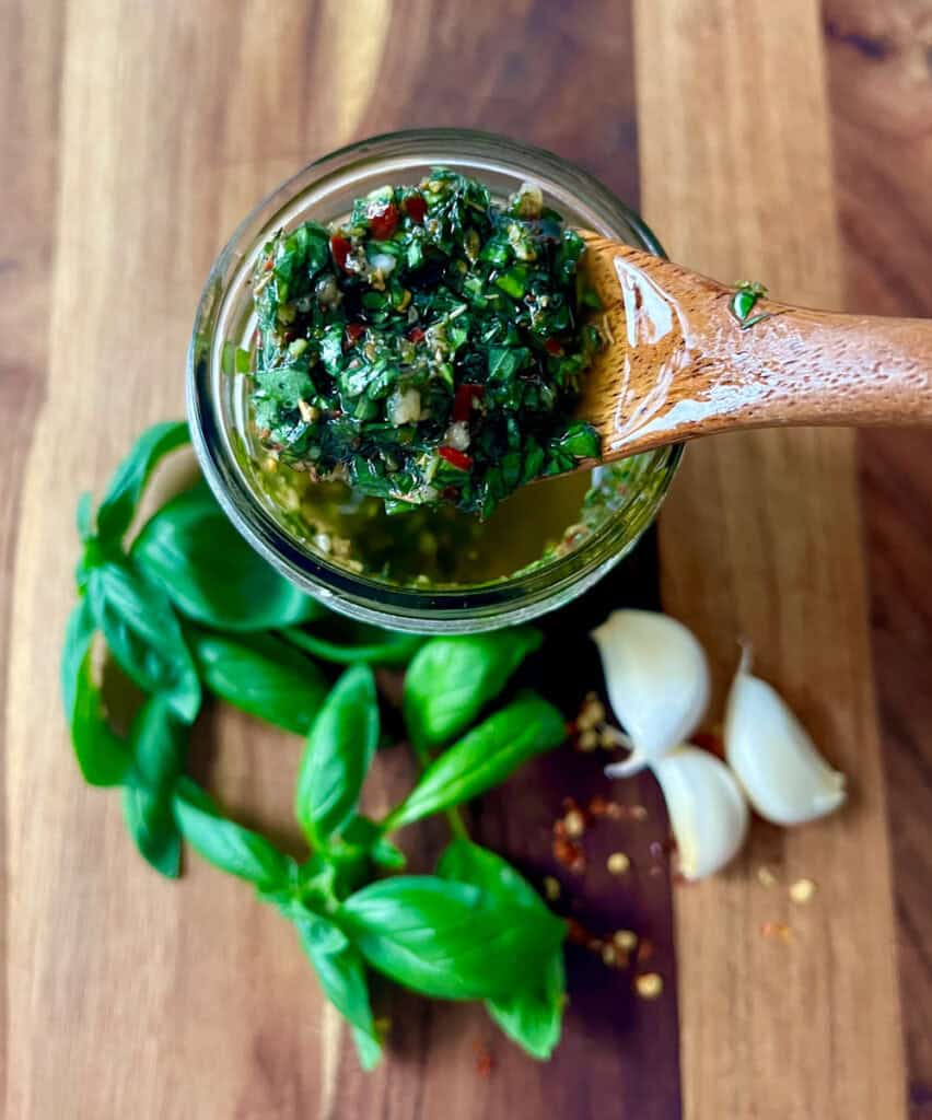 Close-up of basil pesto with garlic and fresh basil leaves on wooden surface.