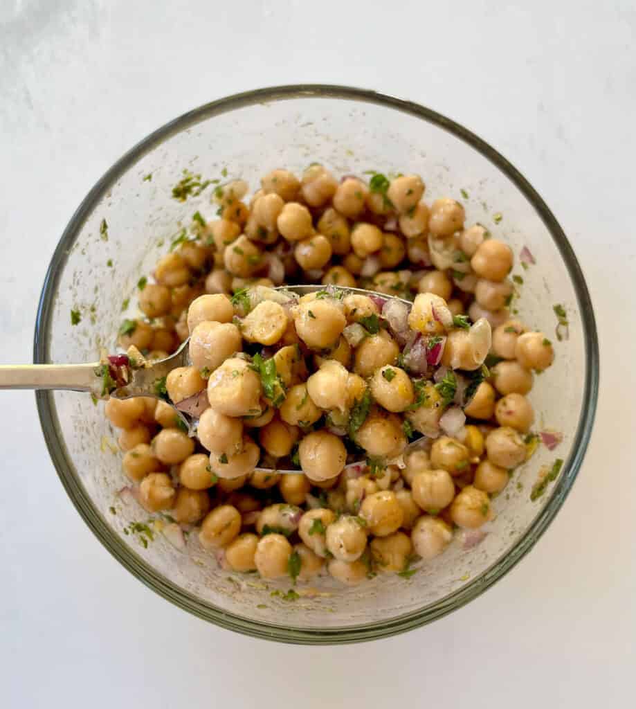 Close-up of marinated chickpeas with herbs and onions in a glass bowl.