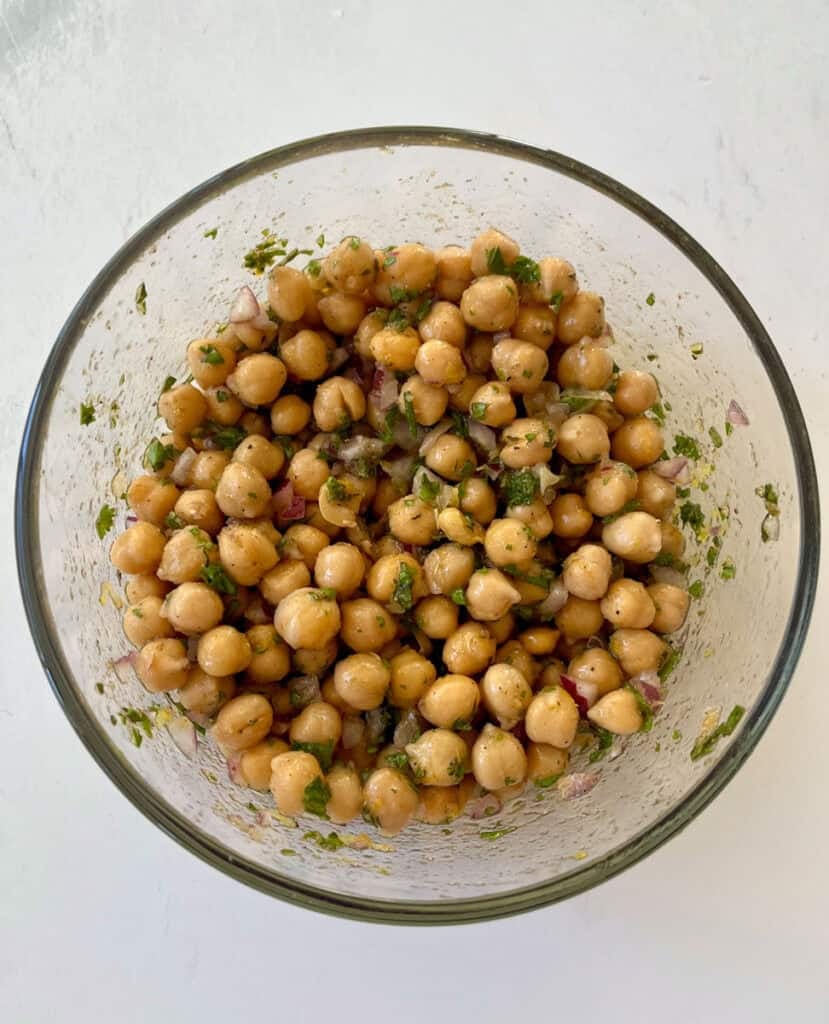 Fresh marinated chickpeas with herbs in a glass bowl on white background.