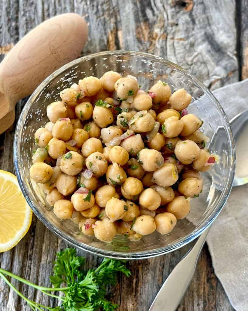 Fresh marinated chickpeas with herbs in a glass bowl on rustic wood table.