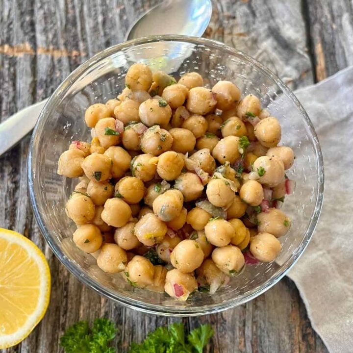 Fresh marinated chickpeas in a glass bowl with lemon and herbs on rustic wood.