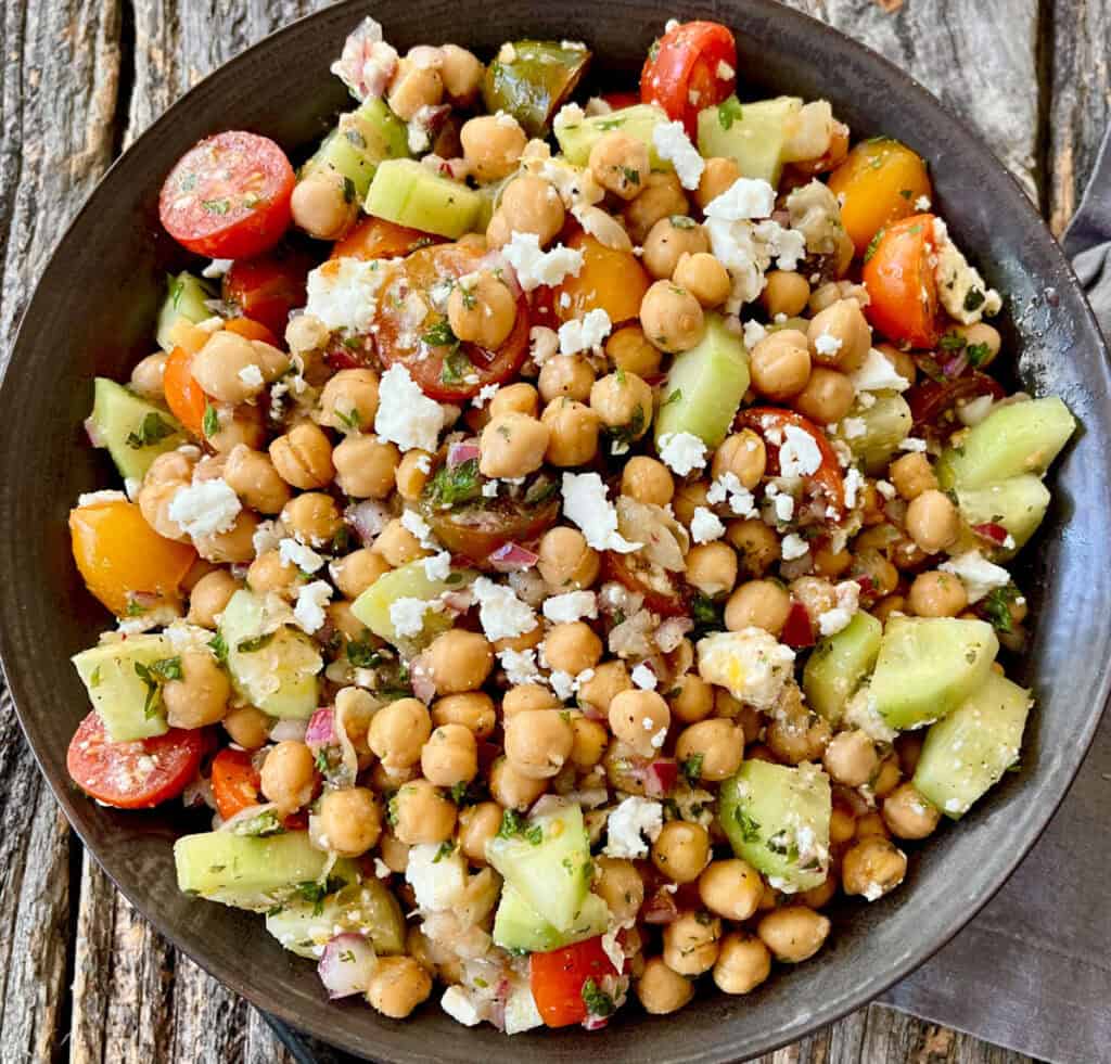 Healthy chickpea and vegetable salad with feta cheese in a black bowl.