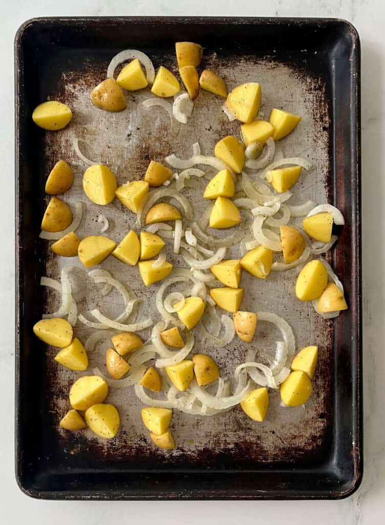 Prepped potatoes and onions on a baking sheet for delicious meal prep.