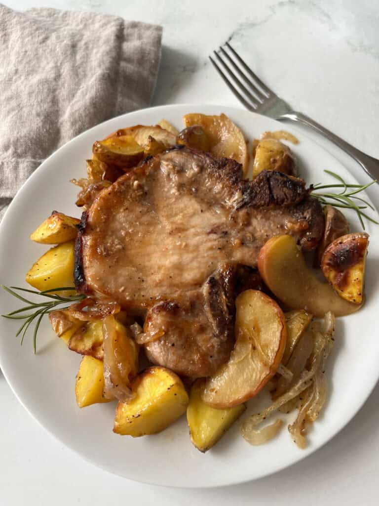 Delicious roast pork served with roasted potatoes, apples, and onions on a white plate.