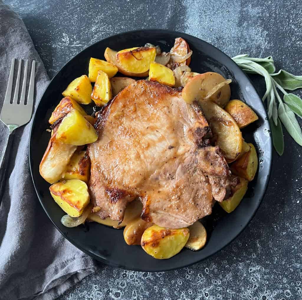 Baked pork chops with crispy potatoes and apples on a black plate.