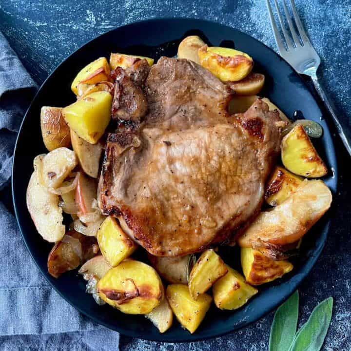 Juicy roasted pork chop served with roasted potatoes and apples on a black plate.