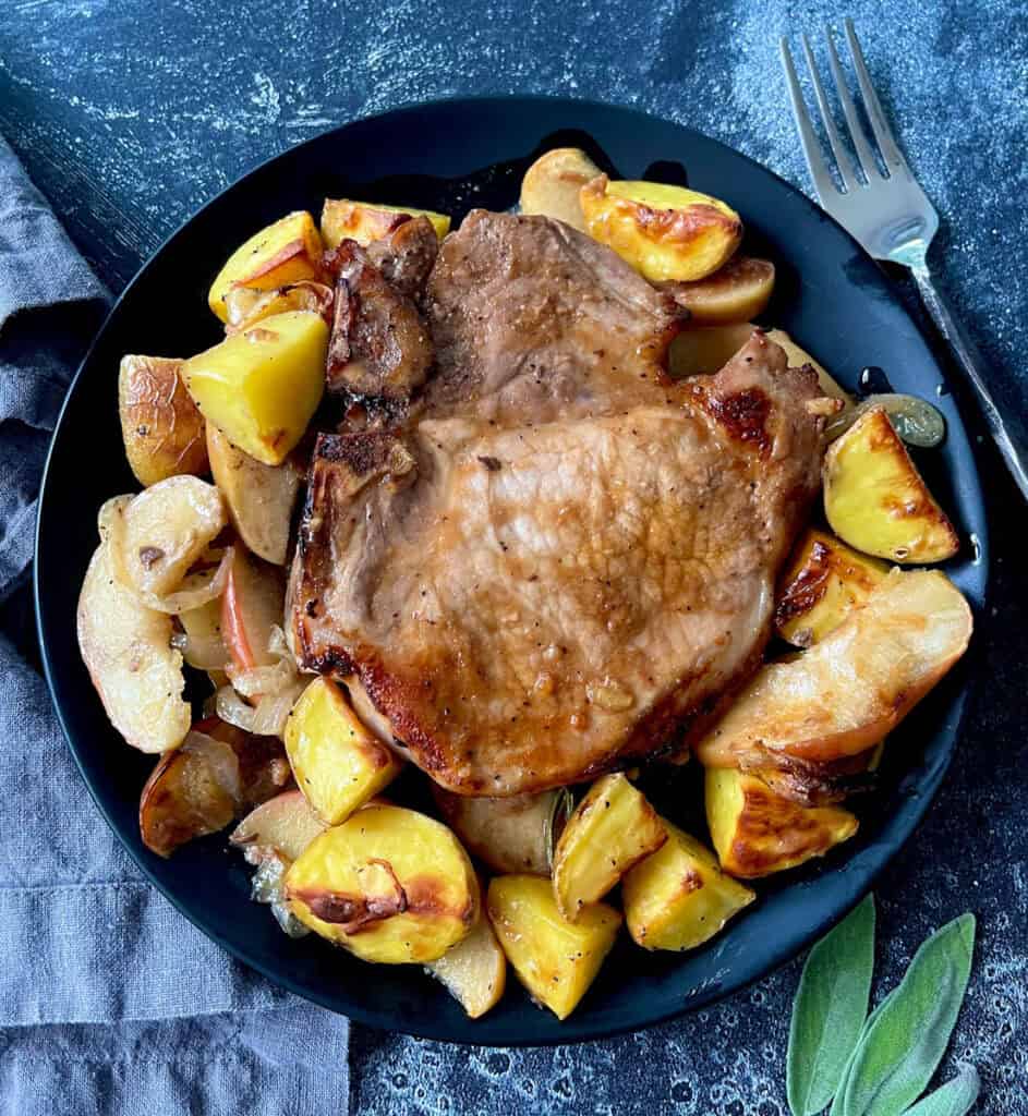 Juicy roasted pork chop served with roasted potatoes and apples on a black plate.