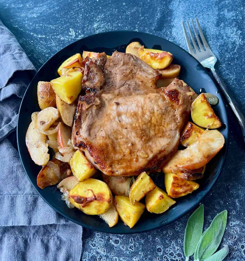 Juicy roasted pork chop served with roasted potatoes and apples on a black plate.